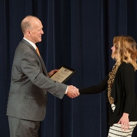 Doctor Potteiger shaking hands with an award recipient in a black sweater and a leopard print scarf